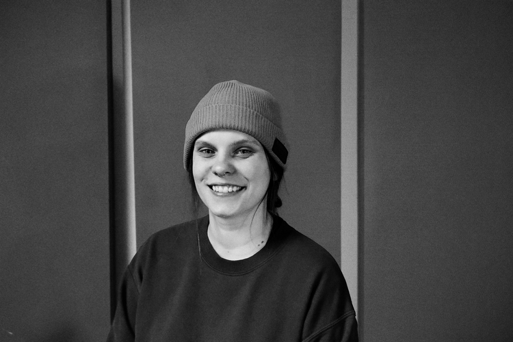 Dani Ramez, photographed in black and white against a studio wall, wearing a beanie and a dark sweatshirt.